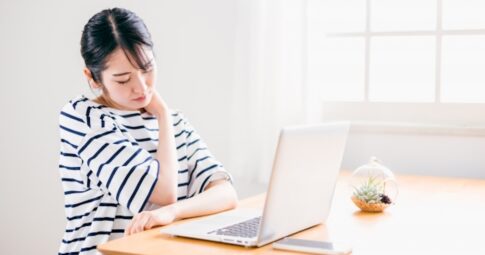 デスクワークのやり過ぎで巻き肩姿勢で肩こりに悩む女性