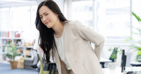 デスクワークをしていて、腰痛に悩むオフィスワーカーの女性